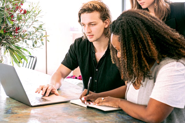 two people at a table one on a laptop one taking notes